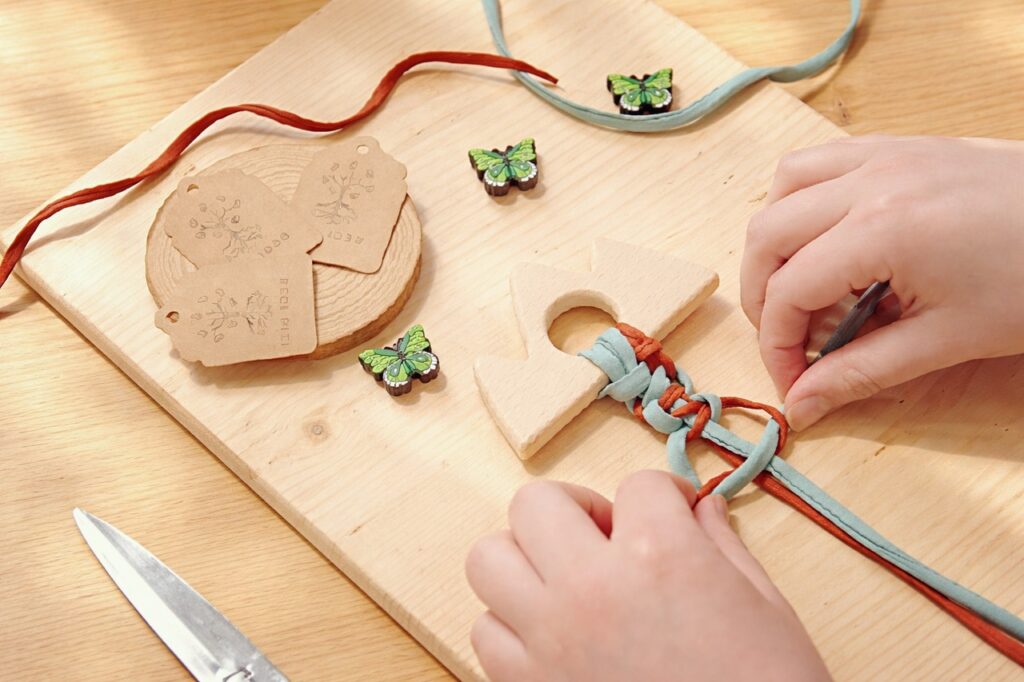 Proceso creativo artesanal de Begi Bizi: manos trabajando con piezas de madera y cordones textiles en un ambiente cálido y natural
