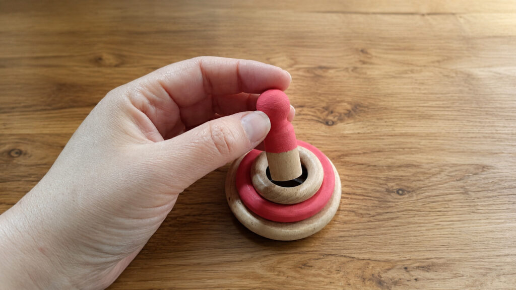 Mano colocando nin dentro de anillas de madera como pieza apilable, propuesta de juego libre para bebés